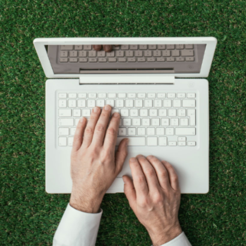 Artificial Turf and Ivy for Commercial Properties showing a man's hands typing on a laptop computer placed on synthetic grass.