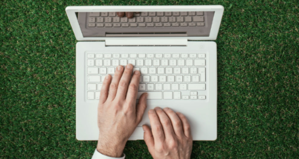 Artificial Turf and Ivy for Commercial Properties showing a man's hands typing on a laptop computer placed on synthetic grass.