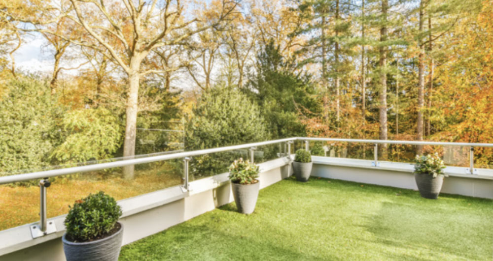 Large corner balcony overlooking a wooded area is enhanced with artificial grass.
